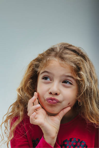 Thoughtful girl with blonde curls wears a vibrant red top, her gestures indicating she's lost in a world of ideas