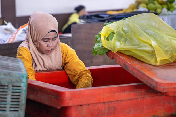 Sandakan, Eastern Borneo, Malaysia - February 19th 2024:  Female greengrocer working at a market stall at the indoor farmer's market