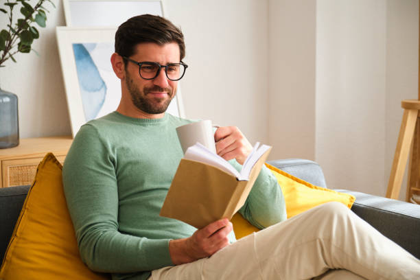 istock A man is sitting on a couch reading a book and drinking coffee. 2152567747