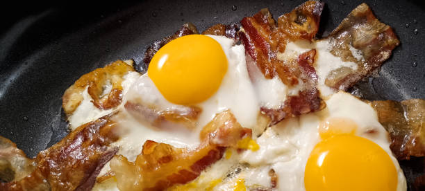 Gourmet Tasty Crunchy Bacon Rashers Freshly Fried With Alluring Juicy Chicken Eggs In Black Ceramic Coated Frying Pan Detail High Resolution Stock Image