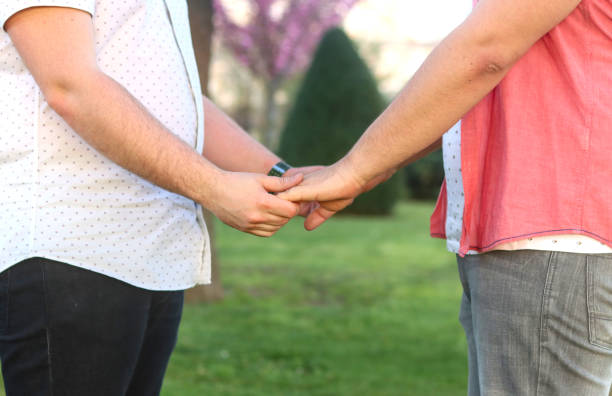 Couple of unrecognizable gay men holding both hands, with a colorful park in the background. LGBT love concept
