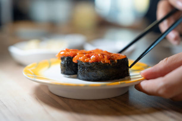 A person using chopsticks to eat sushi served on a plate at a wooden table in a restaurant.
