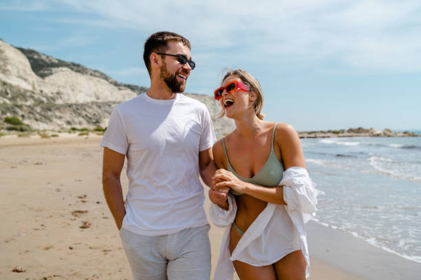 istock Young attractive couple laughs as they walk along the beach 2152596224