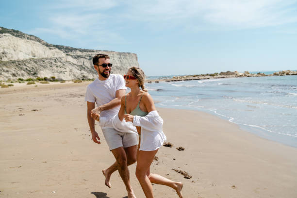 istock Young attractive couple laughs as they walk along the beach 2152596256
