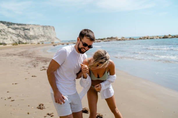 istock Young attractive couple laughs as they walk along the beach 2152596361