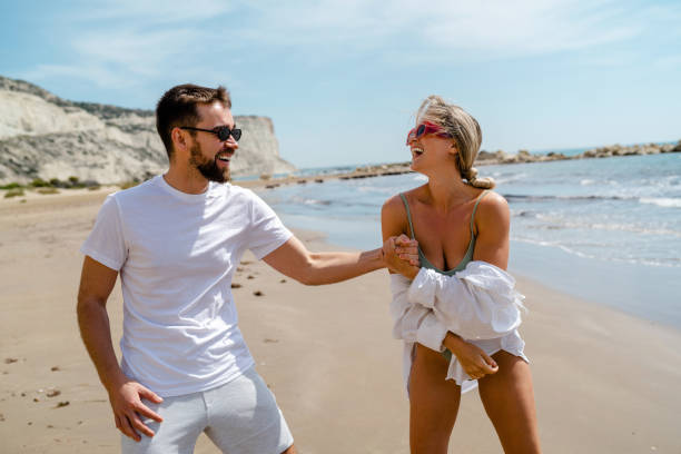 istock Young attractive couple laughs as they walk along the beach 2152596402