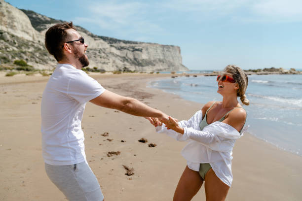istock Young attractive couple laughs as they walk along the beach 2152596481