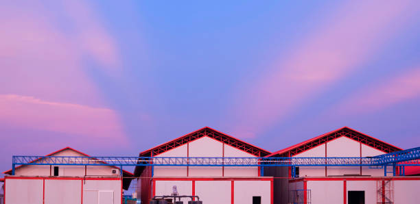 A tall factory building with a ladder on the side. The cargo building is grey and white. The sky is blue