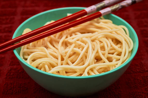 Organic semolina pasta is served in a small teal bowl with red chopsticks over a red kitchen towel