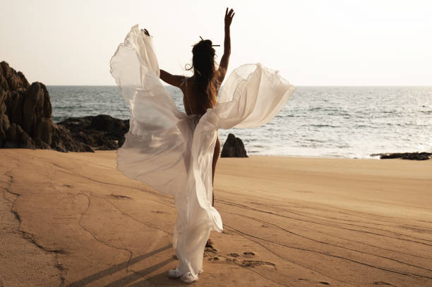 istock Beautiful bride in a flowing white dress dances on the beach 2152603876