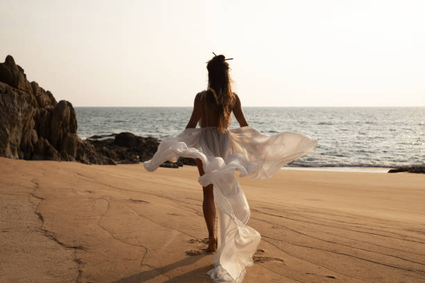 istock Beautiful bride in a flowing white dress dances on the beach 2152604036