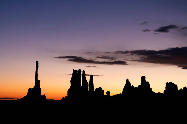 Sunrise behind Monument Valley's famous totem pole and nearby spires, all formed by millions of years of erosion from wind and rain..