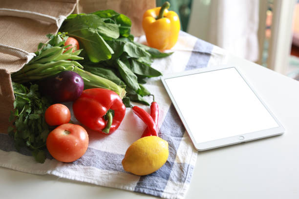 istock A blank screen digital tablet and an eco-friendly reusable shopping bag filled with multi-colored fresh vegetables and groceries on the kitchen counter at home. 2152605373