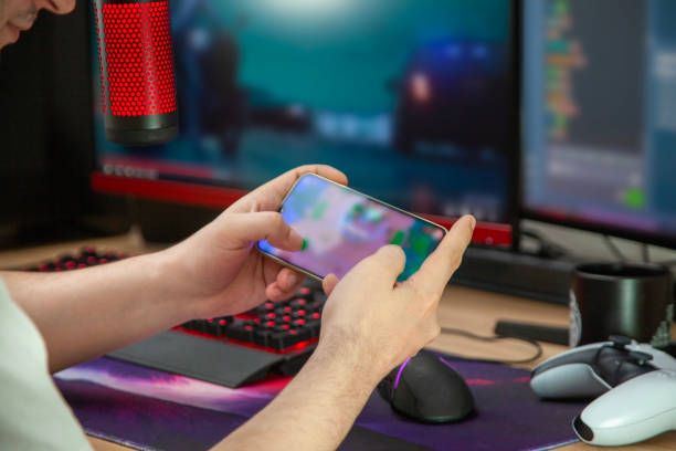 istock Young man play video games with smartphone online in front of computer 2152606934