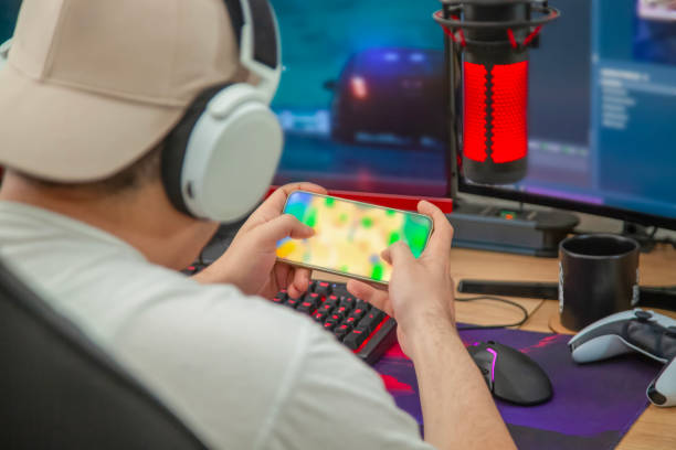 istock Young man play video games with smartphone online in front of computer 2152606957