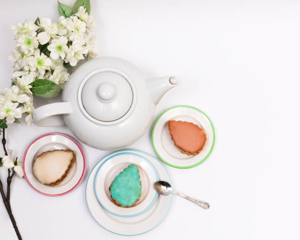 istock Multi-colored cake (turquoise, beige, pink, yellow and caramel) served on saucers around a white teapot on a white background with flowering branches 2152608349