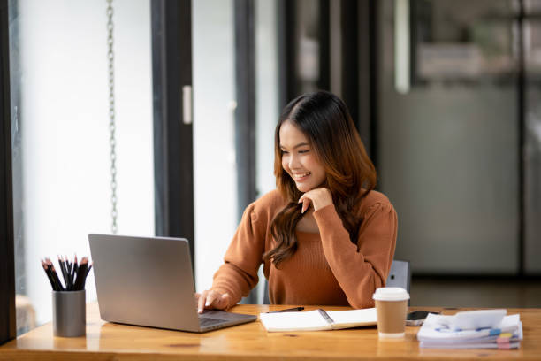 istock A focused young woman working intently at desk with a laptop and notebook in a bright, modern office setting. 2152608837