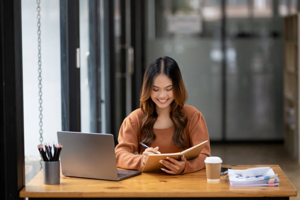 istock A focused young woman working intently at desk with a laptop and notebook in a bright, modern office setting. 2152608919