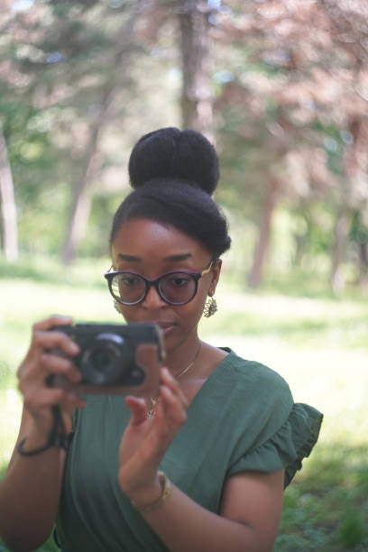 Young black woman taking photos with a compact camera in the park on a sunny day.