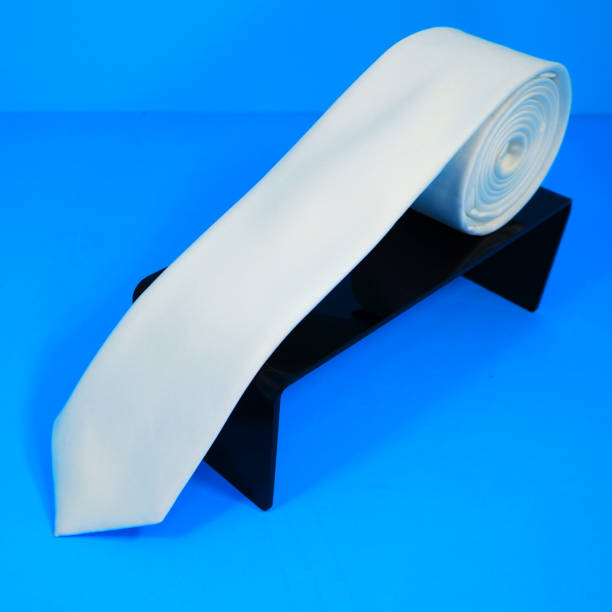 istock Plain fabric white color polyester necktie rolled on black display stand with blue background close-up view single object 2152633715