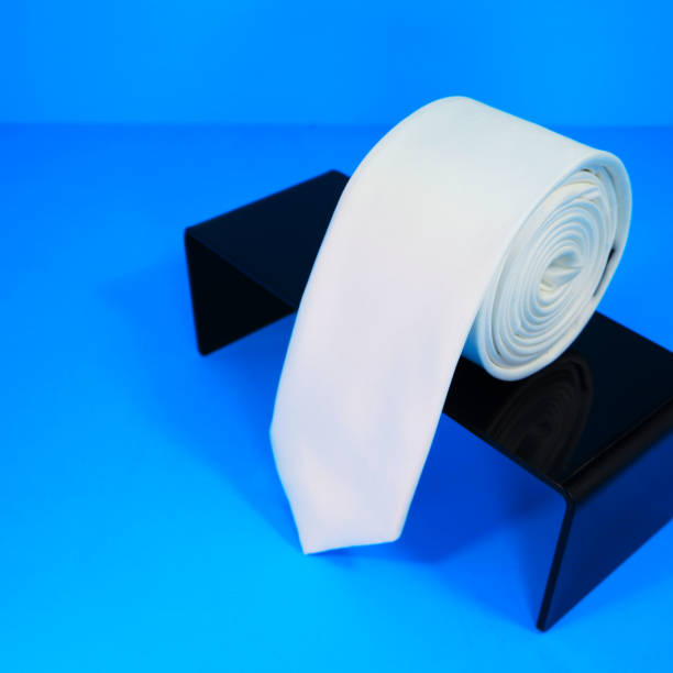 istock Plain fabric white color polyester necktie rolled on black display stand with blue background close-up view single object 2152633946
