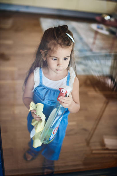 Beautiful small girl helping with chores, cleaning the window.