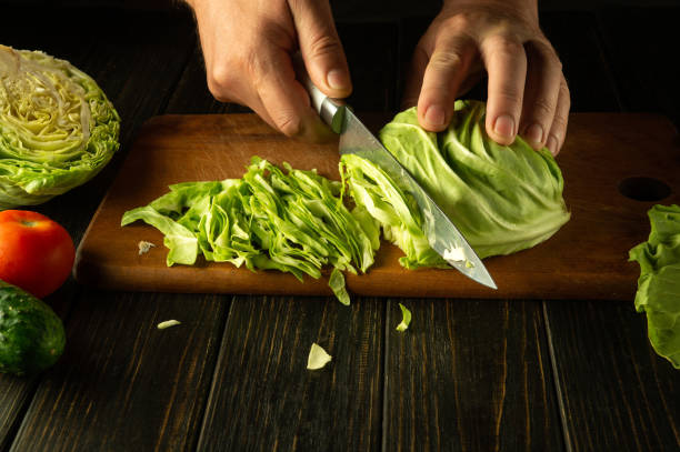istock Cutting cabbage for preparing vegetable salad. The chef hands use a knife to chop fresh cabbage on a kitchen board. Advertising space 2152645752