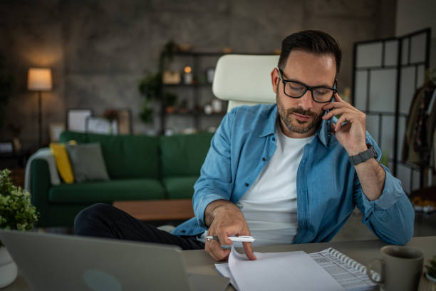 istock Man using mobile phone while working on laptop at home from home office 2152648918