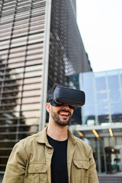 istock A cheerful businessman enjoying a virtual reality experience, wearing VR goggles in a modern cityscape. Concept of multiverse and cyberspace 2152649251