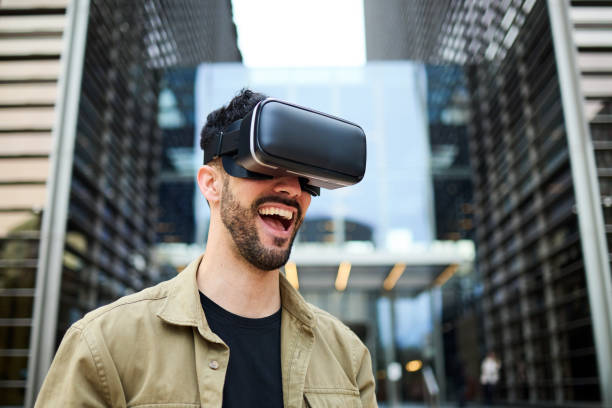 istock A cheerful businessman enjoying a virtual reality experience, wearing VR goggles in a modern cityscape. Concept of multiverse and cyberspace 2152649258