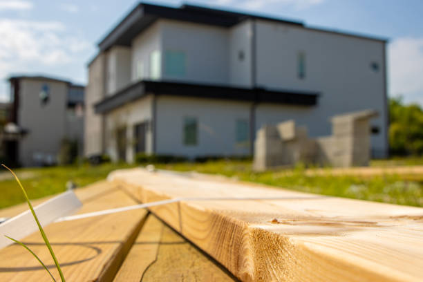Lumber boards for a home construction sit in the foreground with a modern house in the background.
