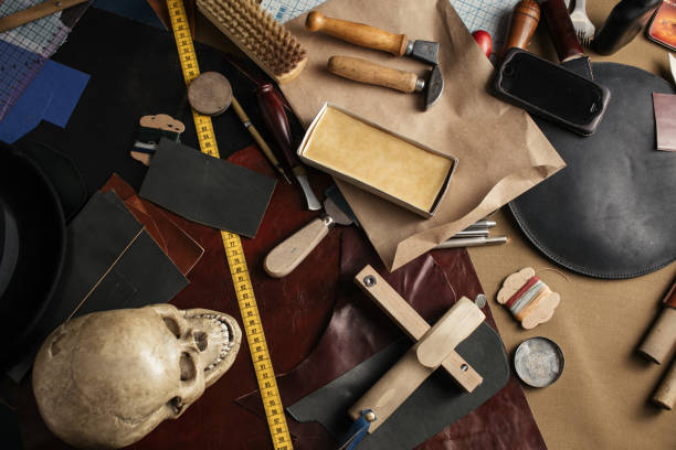 Set of leather craft tools on wooden background. Workplace for shoemaker. Piece of hide and working handmade tools on a work table.
