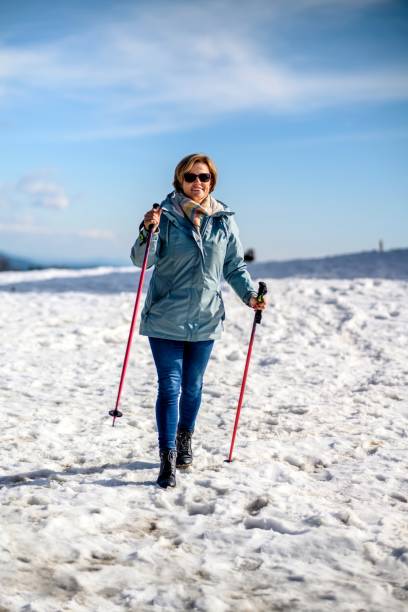 Woman trekking with poles on a grassy mountain path with snow and sun