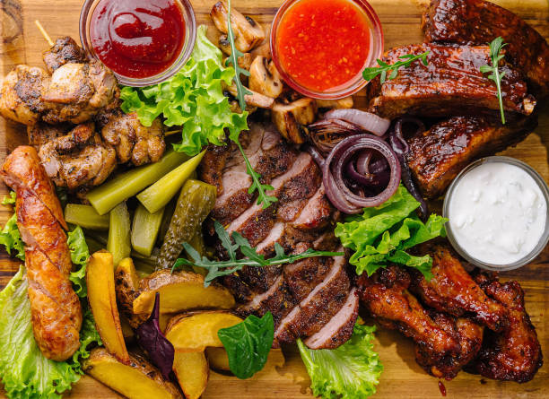 Top view of a delicious bbq feast with dips on a wooden board, surrounded by fresh ingredients