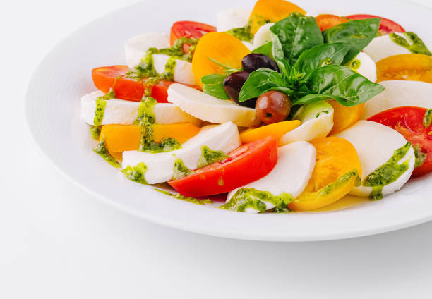 Colorful caprese salad with mozzarella, tomatoes, basil, and pesto dressing on a white plate