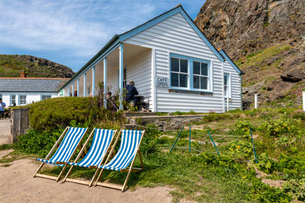Kynance Cove, UK. 11 May 2024. Deckchairs at Kynance Cove Cafe  with people in the cafe.
