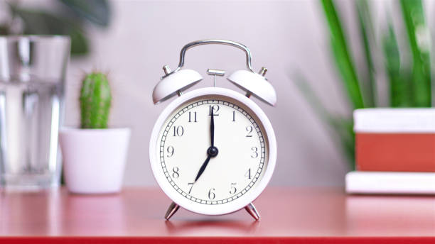 istock Classic white clock on a table. The clock hand points at 07:00, 19:00 close up photo interior 2152702368