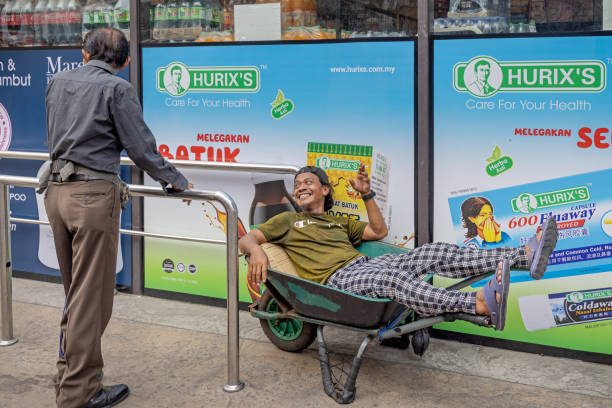 Sandakan, Eastern Borneo, Malaysia - February 12th 2024: Happy young man resting in a wheelbarrow outside the market where he makes business transporting things between the market stalls