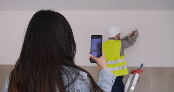 Supervisor captures work progress on smartphone diligent oversight of renovation. Female supervisor documents, ensures quality, efficient work. Oversight focus evident, professional monitoring.