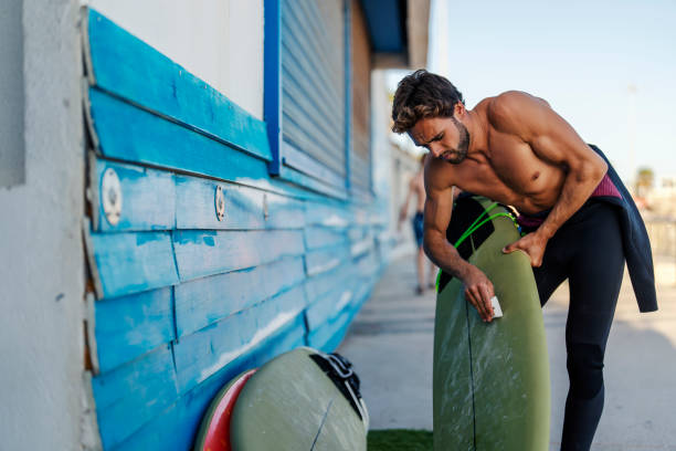 A handsome surfer waxing surfboard.