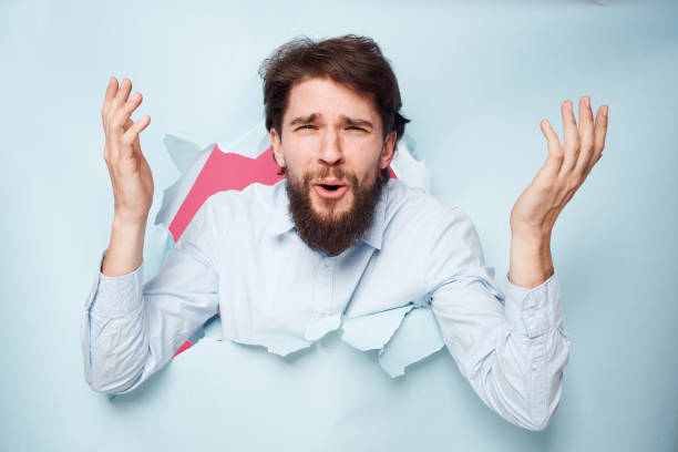 istock Emotional bearded man peeks out from behind the wall in office work shirt 2152734164