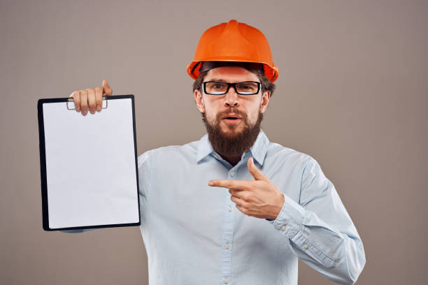 istock Man in orange hard hat professional safety manual documents work 2152736913