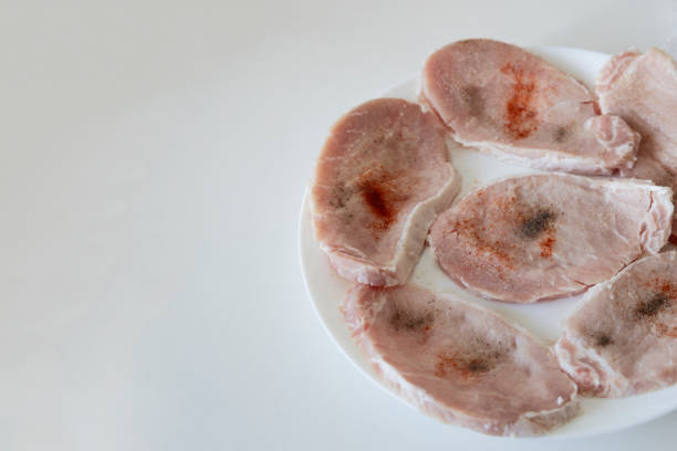 A raw pork chops, cut into pieces and sprinkled with spices on the white plate with copy space