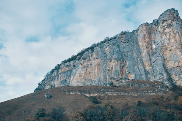 Rear view of a shirtless rock climber high above the ground on the rock face