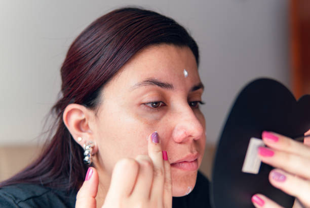 istock young latina applying moisturizer on her face in front of the mirror 2152743170