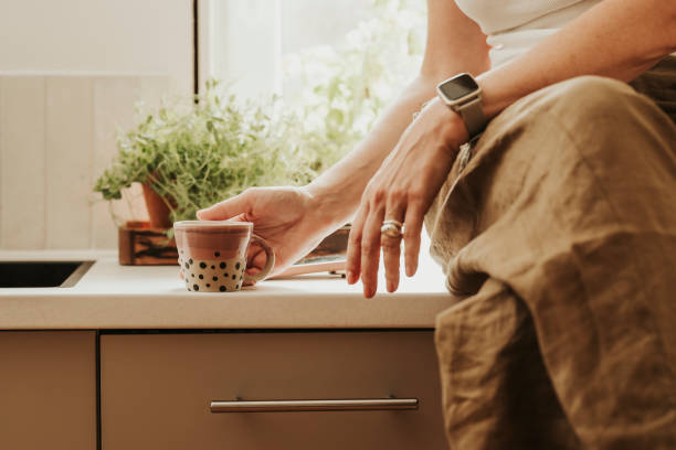 mujer en casa en el interior de su cocina bebiendo café - miembro parte del cuerpo fotografías e imágenes de stock