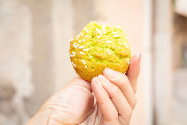freshly backed pistachio biscuit with sugar sticks on top. Woman eats and hold bakery in hand outdoors. Traditional italian cookie in fingers with pastel colours street in background. Close up picture