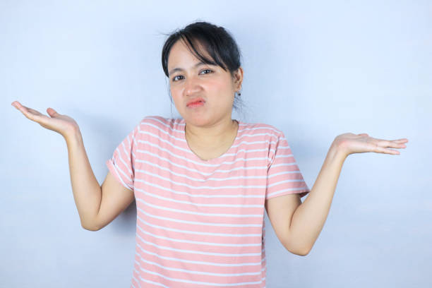I don't know. Unsure asian woman shrugging shoulders over white studio background