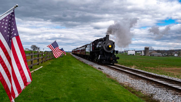 istock A train is traveling down the tracks next to a field with American flags 2152752154