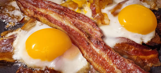 Delicious Gourmet Crunchy Bacon Rashers Freshly Fried With Alluring Juicy Organic Chicken Eggs In Black Ceramic Coated Frying Pan Detail High Resolution Stock Image